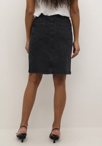 Tummaharmaa farkkuhame, istuva malli, keskipitkä, jossa kaksi takaista taskua ja huolitellut reunat. Yhdistetty mustien korkokenkien kanssa.