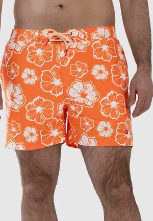 Mann trägt orangefarbene Badeshorts mit weißen Hibiskusblumenmustern und einer vorderen Bindeschnur, gezeigt von der Taille bis zur Mitte des Oberschenkels.