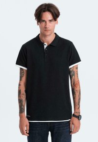 Černé polo tričko s bílým límečkem a krátkými rukávy. Má tříknoflíkovou légu a je vyrobeno z texturované látky.