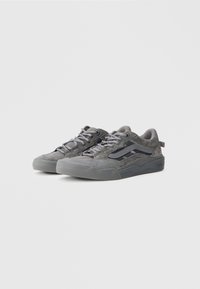 Een paar grijze Vans sneakers met een laag profiel, met details van suede en leer, met vastgebonden veters, gepresenteerd op een effen witte achtergrond.