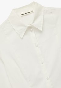 White button-up shirt with pointed collar, fitted seams, and brand label "Olé by Koton" inside collar.