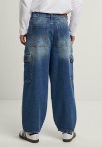 Denim cargo pants with a loose-fit design, featuring a light faded wash, large back pockets, and side cargo pockets.