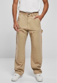 Beige cargobroek van een katoenmix, met meerdere zakken, een losse pasvorm en een metalen knoopsluiting. Gecombineerd met witte sneakers.