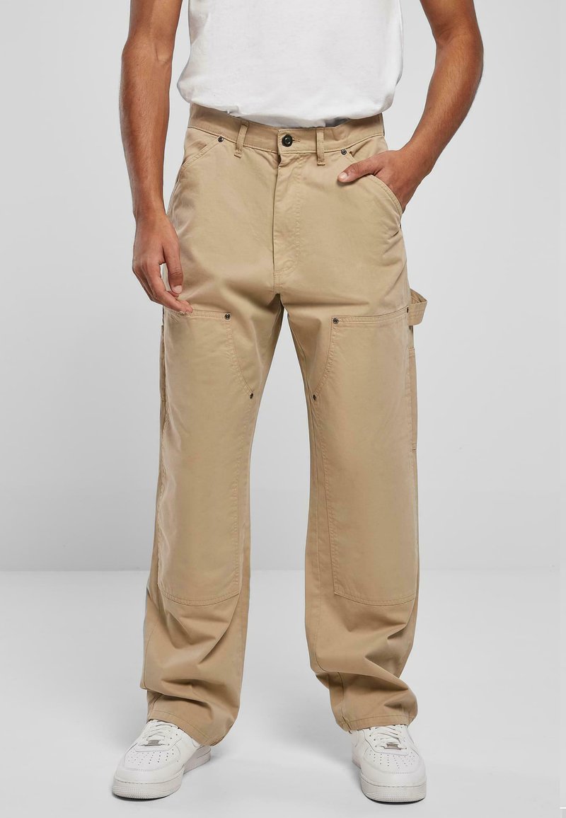 Beige cargobroek van een katoenmix, met meerdere zakken, een losse pasvorm en een metalen knoopsluiting. Gecombineerd met witte sneakers.