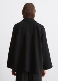 Manteau en laine noir avec une coupe loose, des manches larges et un col rabattu, présentant une texture lisse et un design minimaliste.