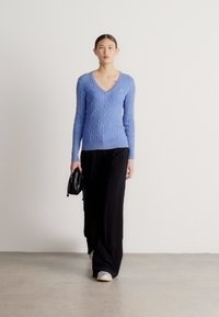 Gaiši zils adīts džemperis ar V veida izgriezumu, kopā ar melnām plašu staru biksēm. Modelis nēsā mazu melnu somiņu un valkā pelēkas sporta kurpes.