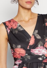 Blommig klänning med djup V-ringning, mörk tyg med rosa och röda rosor, och en texturerad midjedetalj. Mjukt, lätt material.