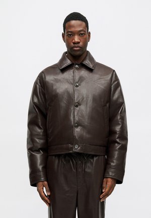 Jachetă din piele maro, scurtă, cu închidere prin butoane în față, guler mare și buzunare laterale. Textură fină cu o strălucire subtilă.