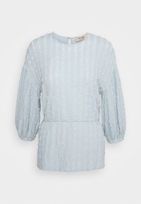Blusa texturizada azul clara com decote redondo, mangas bufantes e cintura justa, apresentando um detalhe em recorte na parte de trás.