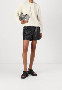 Felpa con cappuccio lavorata a maglia color crema, abbinata a shorts in pelle nera e sandali platform neri. Tieni una piccola borsa argentata.