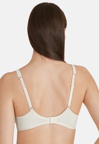 Reggiseno beige chiaro con tessuto a coste, spalline regolabili e bordi ondulati. La chiusura posteriore è dotata di tre ganci per una vestibilità sicura.