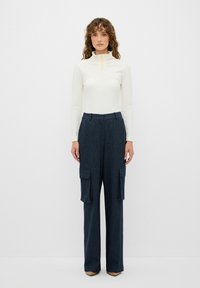 Vitt åtsittande turtleneck med intrikata detaljer vid kragen, ihop med vida marinrandiga cargobyxor med sidfickor.
