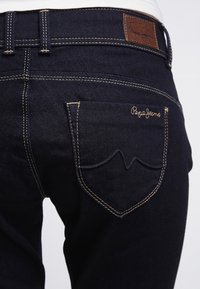 Tmavě modré džíny z denimu s kontrastním švem, zadní kapsa s výšivkou "Pepe Jeans" a koženou značkou na pase.