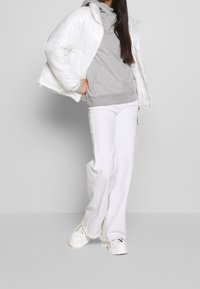 Vit puffjacka med hög krage, grå hoodie under och vita vida byxor. Avslutad med vita chunky sneakers.