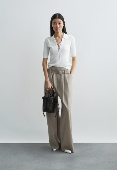 Top branco canelado com decote amarrado, combinado com calças largas bege e uma pequena bolsa de mão preta trançada.