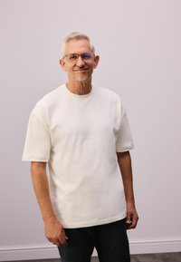 Hvid kortærmet t-shirt lavet af blødt stof, med rund halsudskæring og en afslappet pasform. Båret med mørke bukser, mod en neutral baggrund.