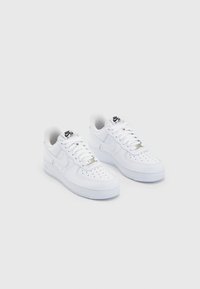 Pair of white Nike Air Force 1 sneakers with perforated toe box, white laces, and black Nike Air logos on tongue, resting on white background.