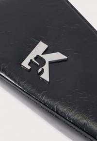 Detailný záber na čiernu textúrovanú koženú peňaženku s strieborným emblémom loga Karl Lagerfeld na prednom rohu.