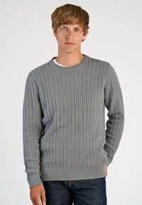 Szary sweter z dzianiny o teksturowanym, kablowym wzorze. Okrągły dekolt oraz ściągacze przy mankietach i u dołu. Noszony na białej koszuli, w zestawieniu z ciemnymi dżinsami.