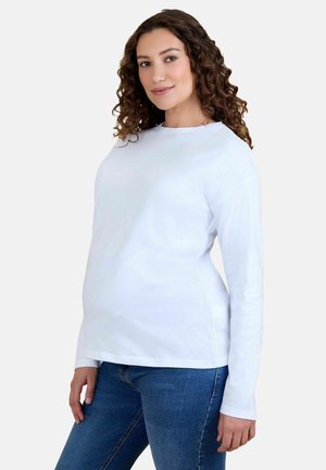 Camisa de algodón blanca de mangas largas con cuello redondo, corte relajado y textura suave. Combinada con jeans de mezclilla azul.