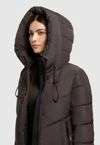 Braune Pufferjacke mit einer großen, gepolsterten Kapuze, verstellbaren Kordeln und mit Reißverschlüssen versehenen Seitentaschen in einem eleganten, gesteppten Design.