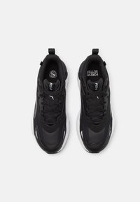 Chaussures de sport noires avec une tige en tissu texturé, un design à lacets et des accents blancs sur la semelle et les côtés. Comprend des sections renforcées au niveau des orteils et du talon.