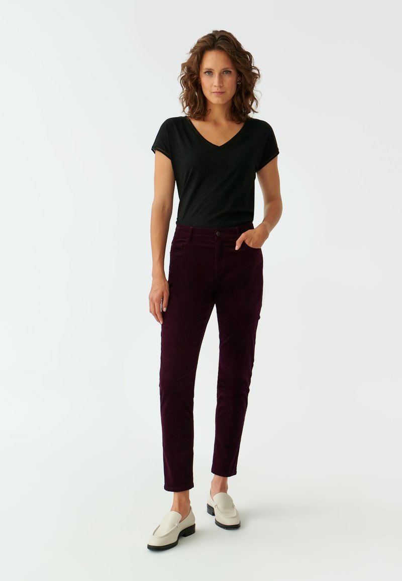 Czarna koszulka typu v-neck, fioletowe spodnie sztruksowe i kremowe buty typu slip-on. Spodnie mają kieszenie i slim fit. Gładka tekstura i subtelny połysk.