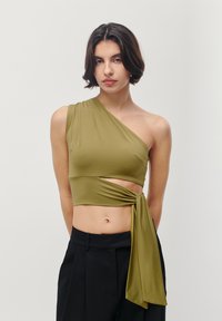 Olive green, one-shoulder crop top with a twist design at the waist, made of smooth fabric. Features a tied accent on the side.