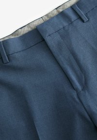 Pantalons bleu marine avec une texture lisse, présentant un devant plat et une doublure de taille à motif gris. Pas de matériel visible.