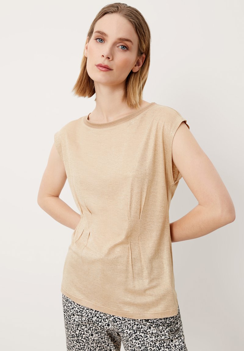 Beige top met korte mouwen, voorzien van een ronde halslijn en een zachte textuur, met een subtiele glans en zijsplijten voor extra detail.