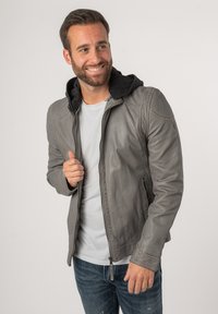 Grijze leren jas met een zwart gevoerde capuchon, voorzien van een ritssluiting aan de voorkant, zijzakken en stikdetails langs de schouders.