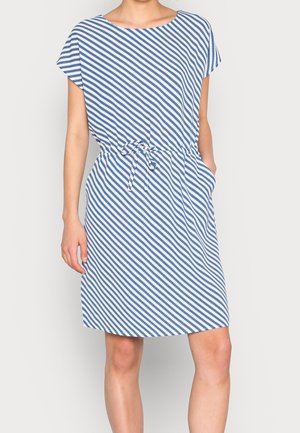 Femme portant une robe bleu et blanc rayée en diagonale au genou, manches courtes et ceinture à la taille, une main dans la poche.