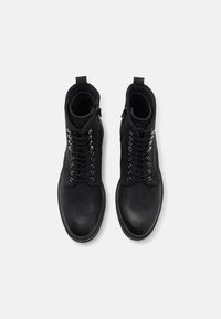 Černé kožené kotníkové boty se strukturovaným povrchem, vybavené kovovými očka, tkaničkami a bočním zipem pro snadné obouvání.