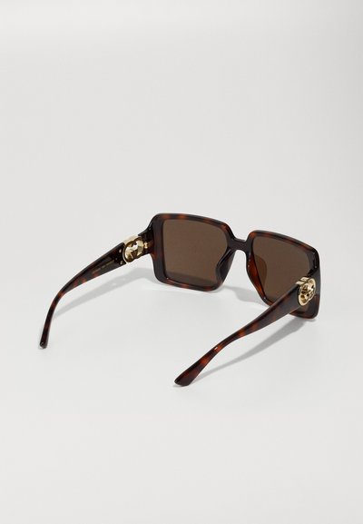 Γυαλιά ηλίου σε καφετί κελύφος με τετράγωνα καφέ φακοί. Χρυσές λεπτομέρειες στη βίδα του σκελετού, με λογότυπο. Λείος, γυαλιστερός φινίρισμα.