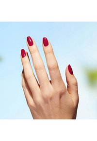 Hand mit mittelgroßen, mandelförmigen Nägeln, die mit glänzendem, dunkellackiertem Rot überzogen sind, vor einem hellblauen Hintergrund. Glatte Hauttextur sichtbar.
