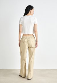 Witte, geknipte t-shirt gecombineerd met lichtbeige cargo broek met elastische taille en zakken, in een ontspannen pasvorm, van achteren weergegeven.