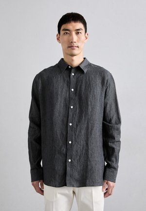 Mörkgrå linneskjorta med långa ärmar, knappad krage och vita knappar. Har en avslappnad passform och textil med en något rynkad struktur.