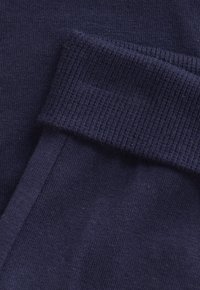 Navyblauwe stof met een gladde textuur; heeft een geribde manchette en is strak geweven. Een close-up van de oppervlakdetails van het materiaal.