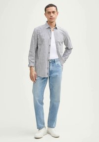 Chemise à rayures gris et blanche, portée sur un débardeur blanc, associée à un jean bleu clair et des baskets blanches.