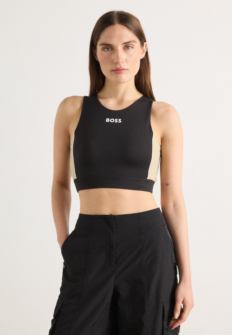 Top corto nero con pannelli laterali beige, texture liscia, collo rotondo e logo "BOSS" in bianco sul davanti. Adatto per abbigliamento sportivo.
