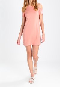 Różowa sukienka z krótkim rękawem i wyciętymi ramionami, wykonana z miękkiego materiału. Połączona z beżowymi sandałami na płaskiej podeszwie. Prosty, luźny krój.