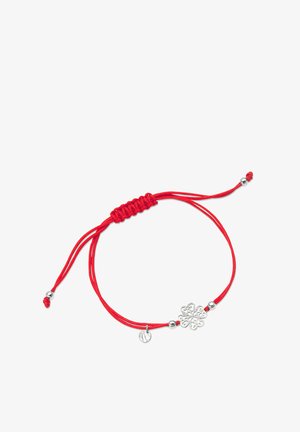 Czerwona bransoletka z sznurkiem, ozdobiona srebrnym kwiatowym zawieszką oraz małą okrągłą etykietką. Sznurek jest regulowany, z metalowymi koralikami przy zapięciu.