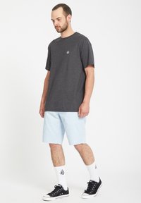 Gray short-sleeve T-shirt with a logo on the chest, paired with light blue shorts, white socks, and black sneakers. Simple design.