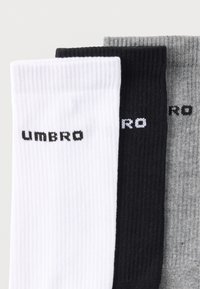 Tre par sokker i hvid, sort og grå. Hver har en ribbet tekstur med "UMBRO" branding i kontrastfarver sort eller hvid.