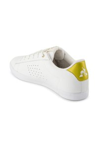 Sneaker bianca in pelle con perforazioni sui lati, un tocco di giallo sul tallone e una suola in gomma bianca. Punta rinforzata e occhielli dorati.