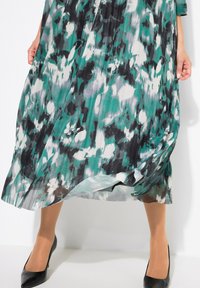 Robe fluide jusqu'aux chevilles avec imprime floral vert, noir et blanc. Fabriquée en tissu léger, elle présente une texture plissée et une coupe ample.