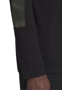 Zwart shirt met lange mouwen en een gestructureerde accentstreep in legergroen. Voorzien van een rechte snit, een ronde halslijn en naadloze boorden.