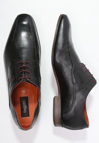 Chaussures en cuir noir au design élégant, bouts pointus, accents marron et détail de lacets rouges. Intérieur avec doublure orange et bords cousus.