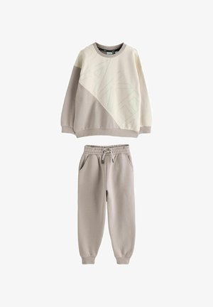 Jasnobeżowa bluza z ukośnym wzorem i napisem „BAKER”, zestawiona z pasującymi joggerami z elastycznym paskiem w podobnym odcieniu.