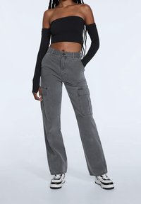 Graue Cargo-Hosen mit lockerer Passform, hoher Taille, zwei großen Seitentaschen und glatter Stoffstruktur. Kombiniert mit einem schwarzen Crop-Top.